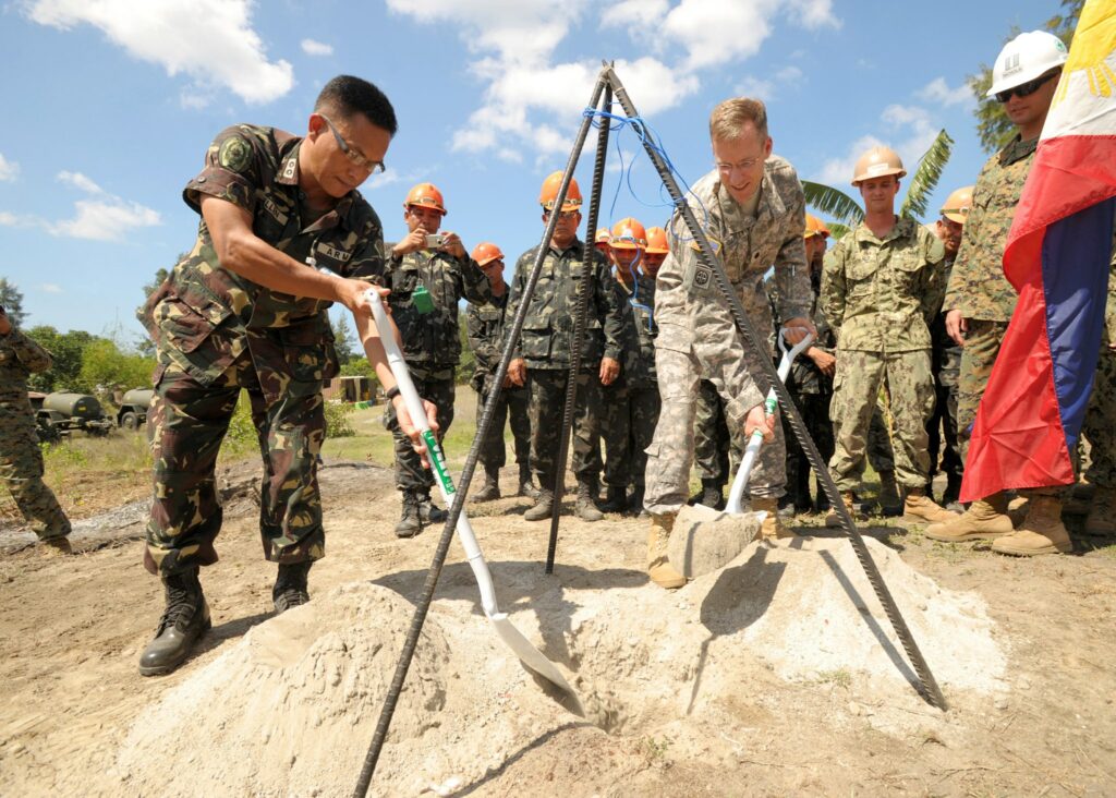Visiting Forces Agreement."Philippine army Lt. Col. Henry Bellan, left, and U.S. Army Lt. Col. John Garrity, the deputy commanders of Joint Civil Military Operations Task Force, bury a time capsule containing the construction plans for a footbridge during a groundbreaking ceremony March 18, 2013, in San Narciso, Philippines. The job was one of eight engineering civic action projects conducted by U.S. and Philippine service members in support of exercise Balikatan 2013. Balikatan is an annual bilateral training exercise designed to increase interoperability between the Armed Forces of the Philippines and the U.S. military when responding to future natural disasters. (DoD photo by Mass Communication Specialist 1st Class Chris Fahey, U.S. Navy/Released)" by MC1 Chris Fahey is in the Public Domain
