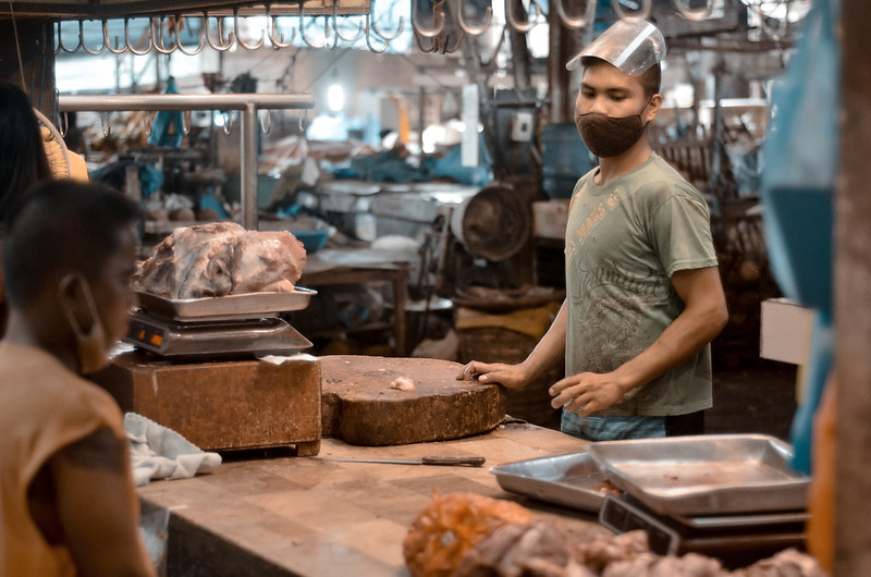 "THE BURGOS BUTCHER. A meat vendor tends to a buyer at the wet section of the Burgos Public Market in Bacolod City, Philippines on Monday, 12 October 2020, two days after the city government implemented a mass testing program." by Rodney A. Jarder Jr., DNX News is licensed under CC BY-SA 2.0