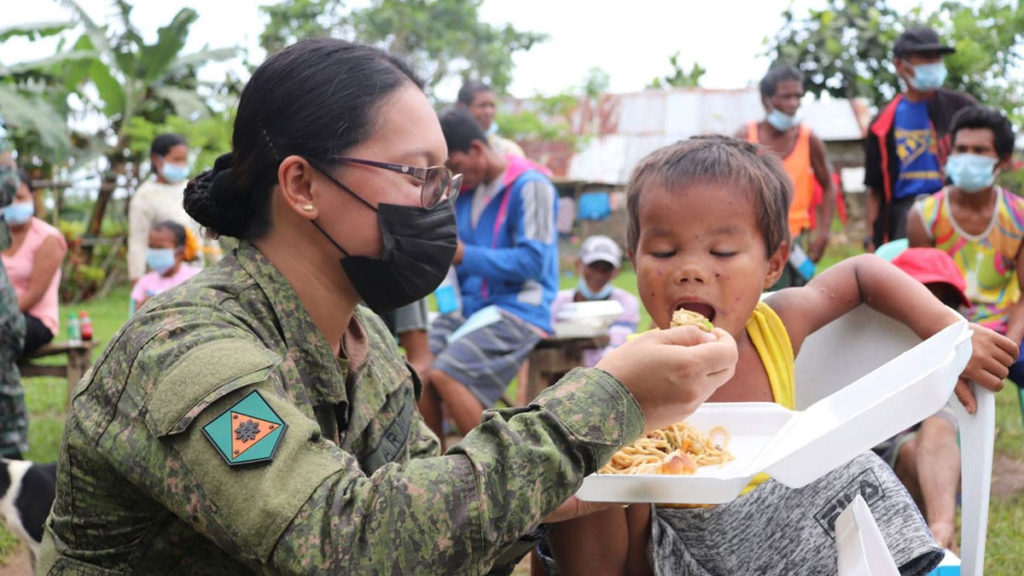 A trooper of the 79th Infantry Battalion of the Philippine Army feeds a child during an outreach activity with indigenous peoples of the Ata and Bukid on tribes in the upland village of Minapasok in Calatrava town this month. | Photo courtesy of 79 Infantry Battalion.