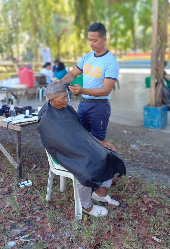 A police personnel provides free haircut to an elderly man.